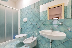 Un baño con ducha, dos inodoros, un bidé y un lavabo.