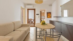 A modern living room with a sofa, a round dining table with a chair, and a kitchen area with cabinets and a large mirror.