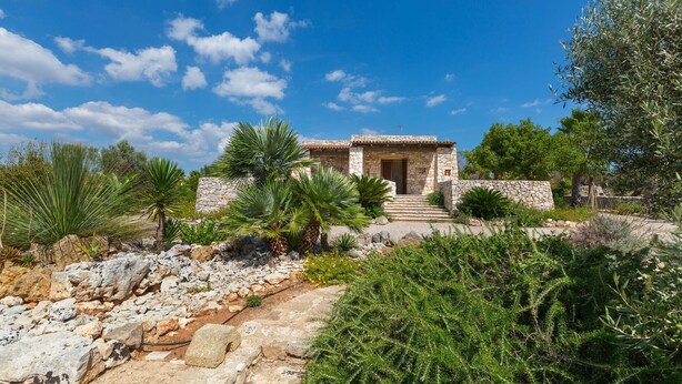 A stone building with a tiled roof, surrounded by greenery and a stone pathway leading to the entrance. - Villa Mila (Morciano di Leuca)