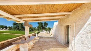 An outdoor patio with stone flooring, wooden benches, and a pergola structure. - Trullo Giamar (Ostuni)