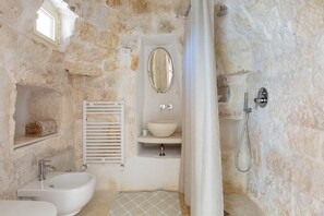 A stone-walled bathroom with a white sink, a mirror, and a shower. - Trullo Giamar (Ostuni)