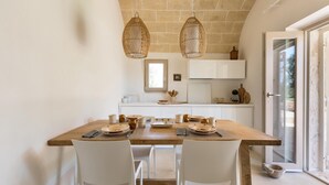 A dining area with a wooden table set for two, white chairs, and hanging wicker light fixtures. - Trullo Giamar (Ostuni)
