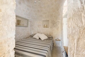 A stone-walled bedroom with a bed, a small table, and a wall-mounted mirror. - Trullo Giamar (Ostuni)