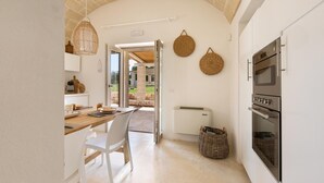A kitchen with white cabinets, a built-in oven, and a dining area with a white table and chairs. - Trullo Giamar (Ostuni)