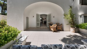 A courtyard with a white wall, an arched entrance, wicker furniture, and potted plants. - Masseria Villa (Melendugno)