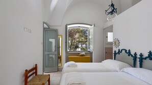 A bedroom with two beds, a wooden chair, a yellow dresser, and a window with a view of trees. - Masseria Villa (Melendugno)