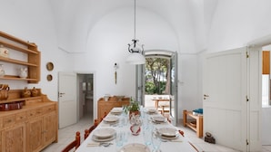 A dining area with a long table set for six, surrounded by wooden cabinets and a hanging light fixture. - Masseria Villa (Melendugno)
