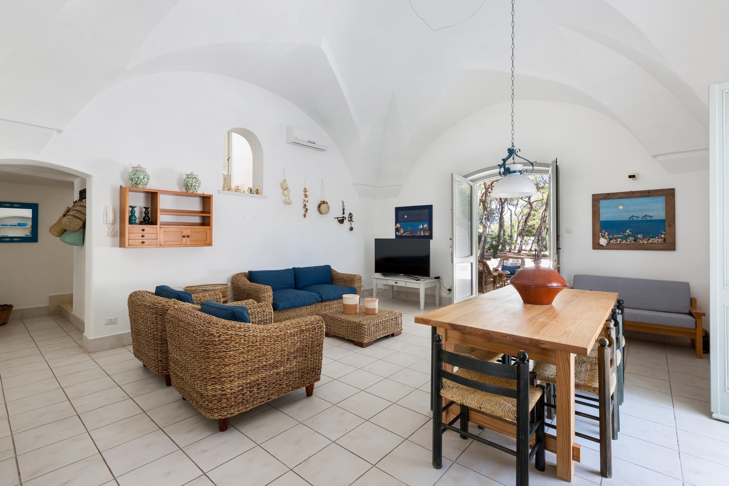 A spacious living area with wicker furniture, a wooden dining table, and a television.