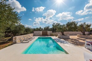 Une piscine rectangulaire avec un mur en pierre d’un côté et des chaises longues disposées tout autour.
