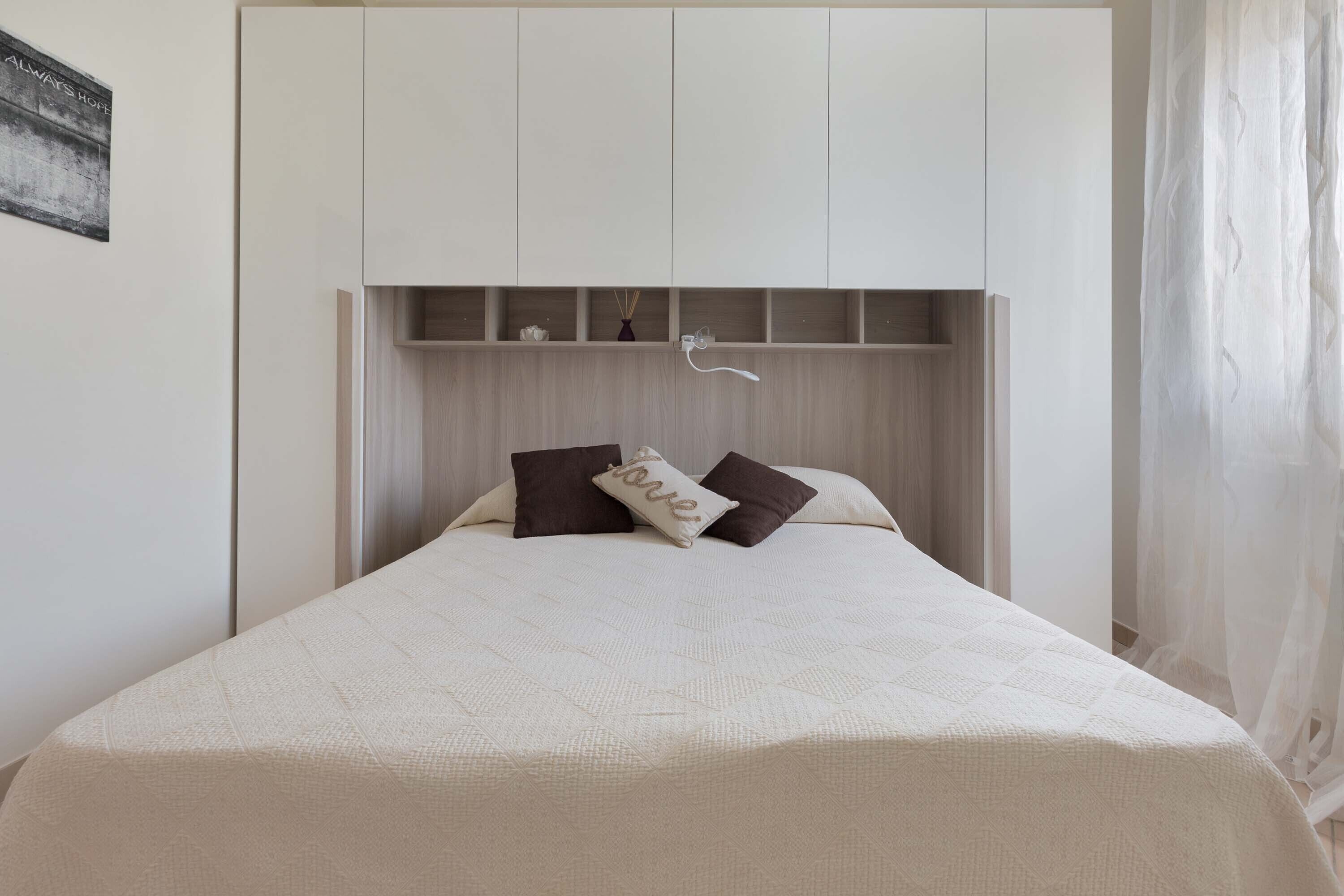 A bedroom with a bed, a headboard with shelves, and a wall-mounted light fixture.