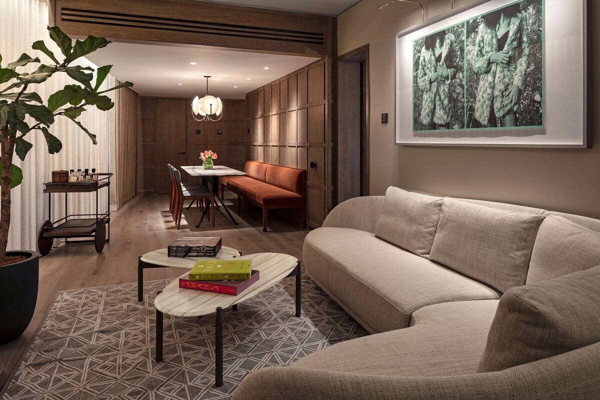 A modern living room with a sofa, a coffee table with books, a dining area with a bench, and a large plant.