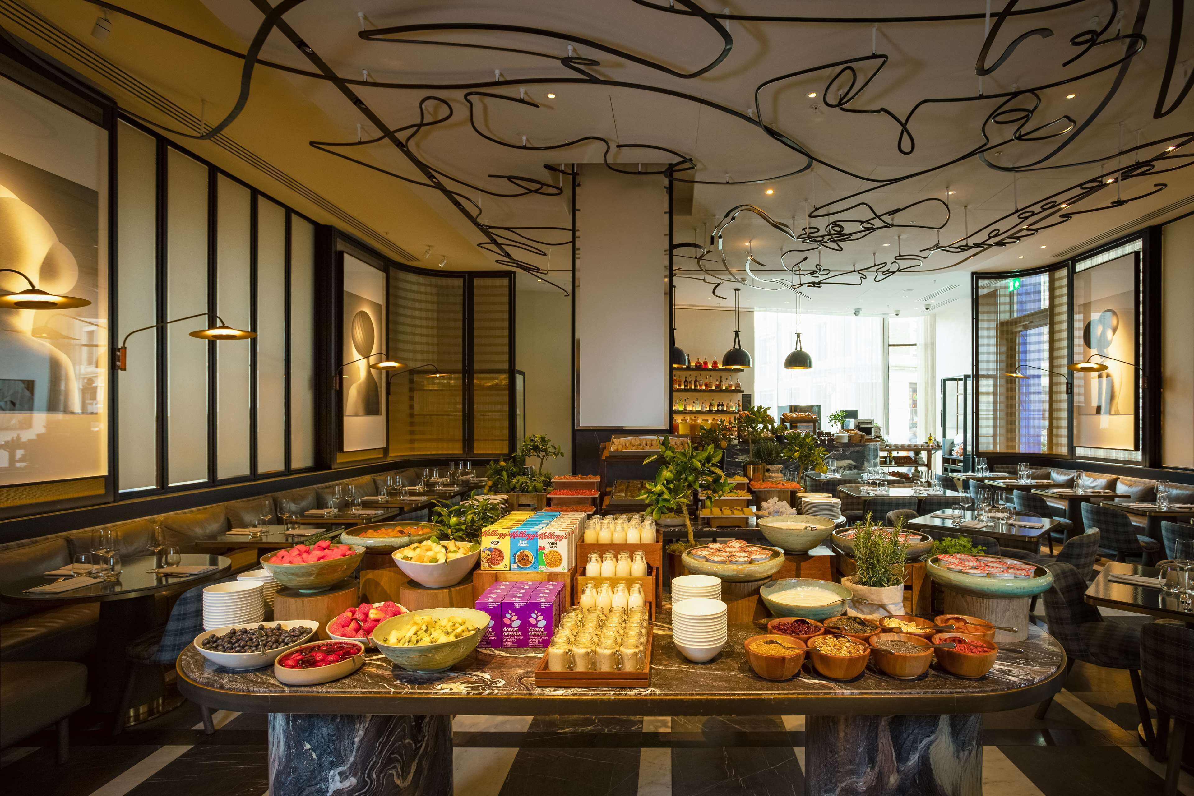 A buffet setup with various food items and beverages, surrounded by seating areas and a modern interior design.