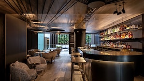 Un'area bar moderna con pavimento in legno, sgabelli da bar e una scaffalatura ben fornita di liquori.