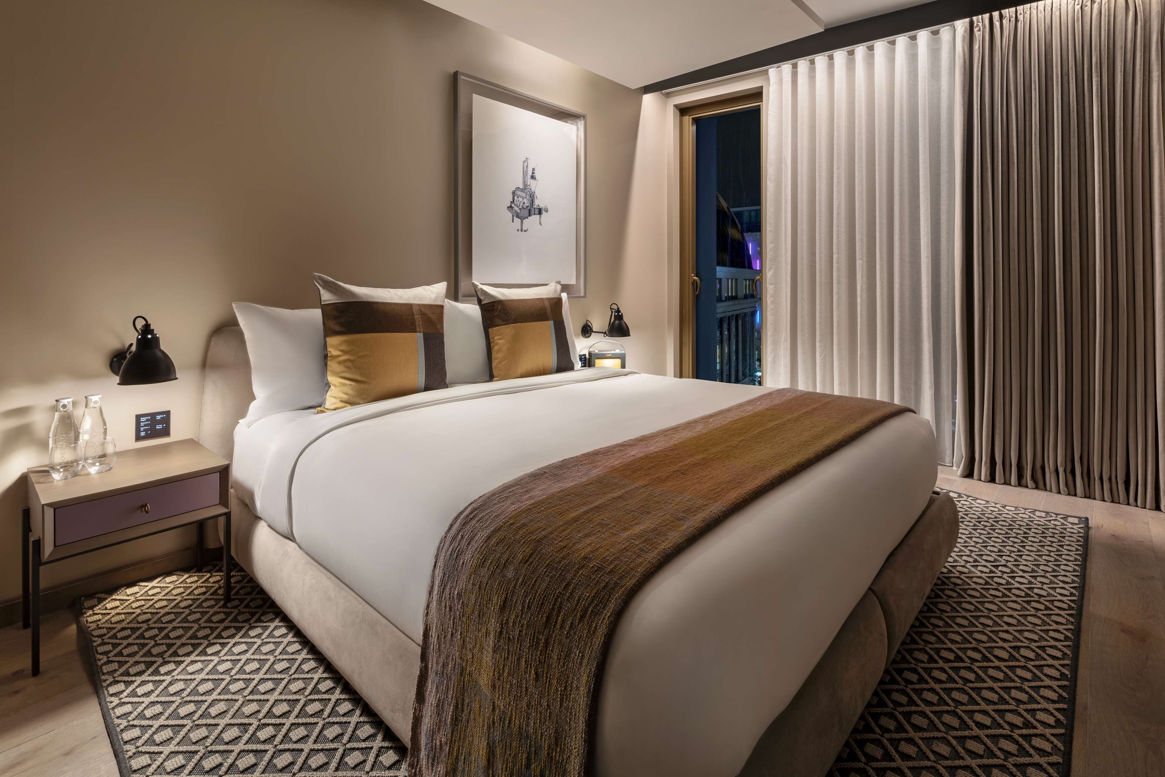 A hotel room with a large bed, a nightstand with a lamp, and a window with curtains.