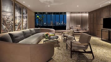 Una sala de estar moderna con un sofá modular grande, una mesa de centro de vidrio y un sillón cómodo. Un televisor de pantalla plana está montado en la pared, y la habitación cuenta con un ventanal con vistas a la ciudad.