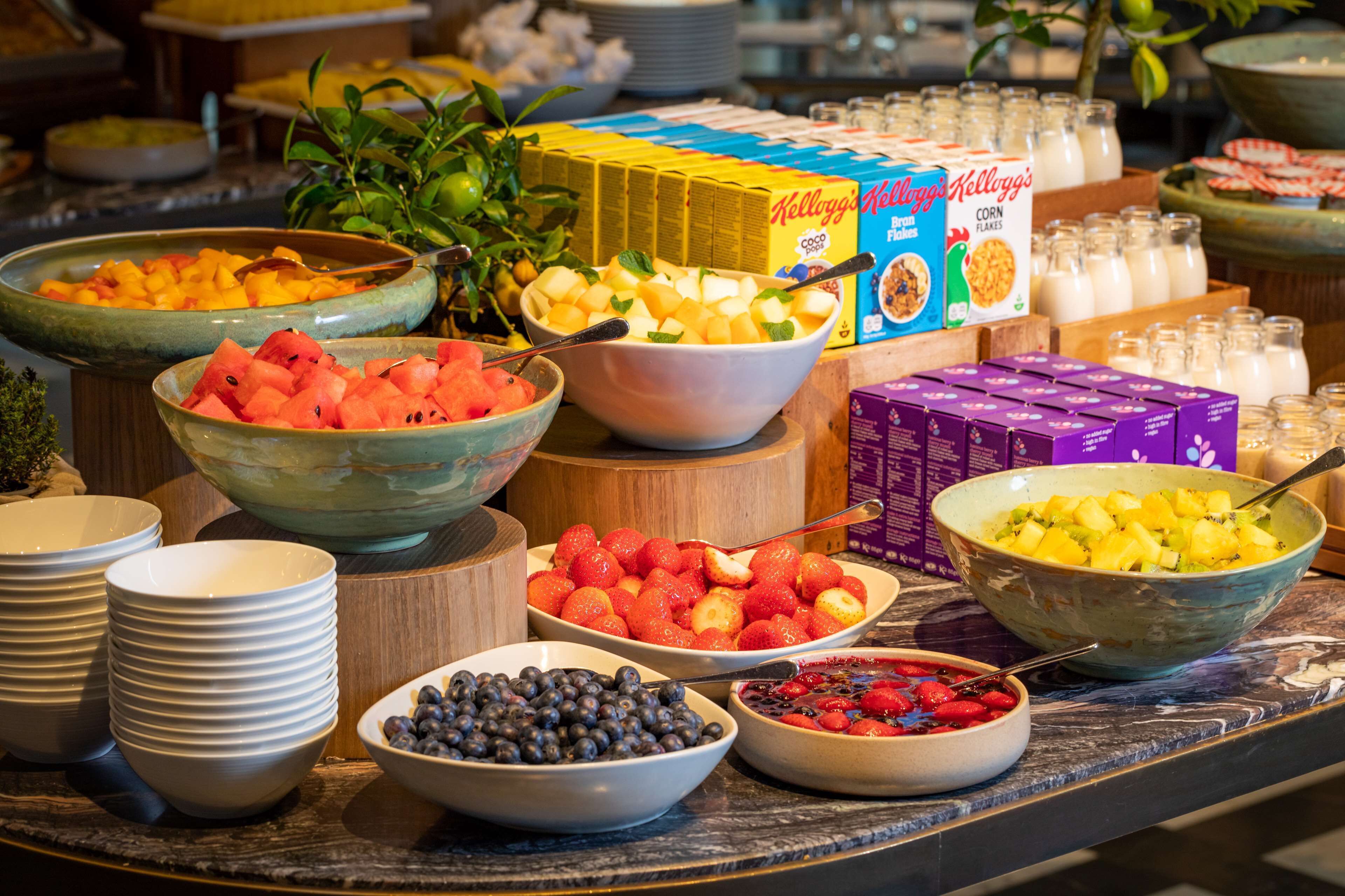 A buffet table with various bowls of fruits and cereals.