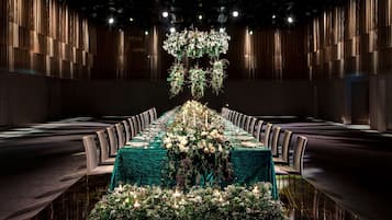 A long banquet table with a green tablecloth, surrounded by chairs, and decorated with floral arrangements and candles.