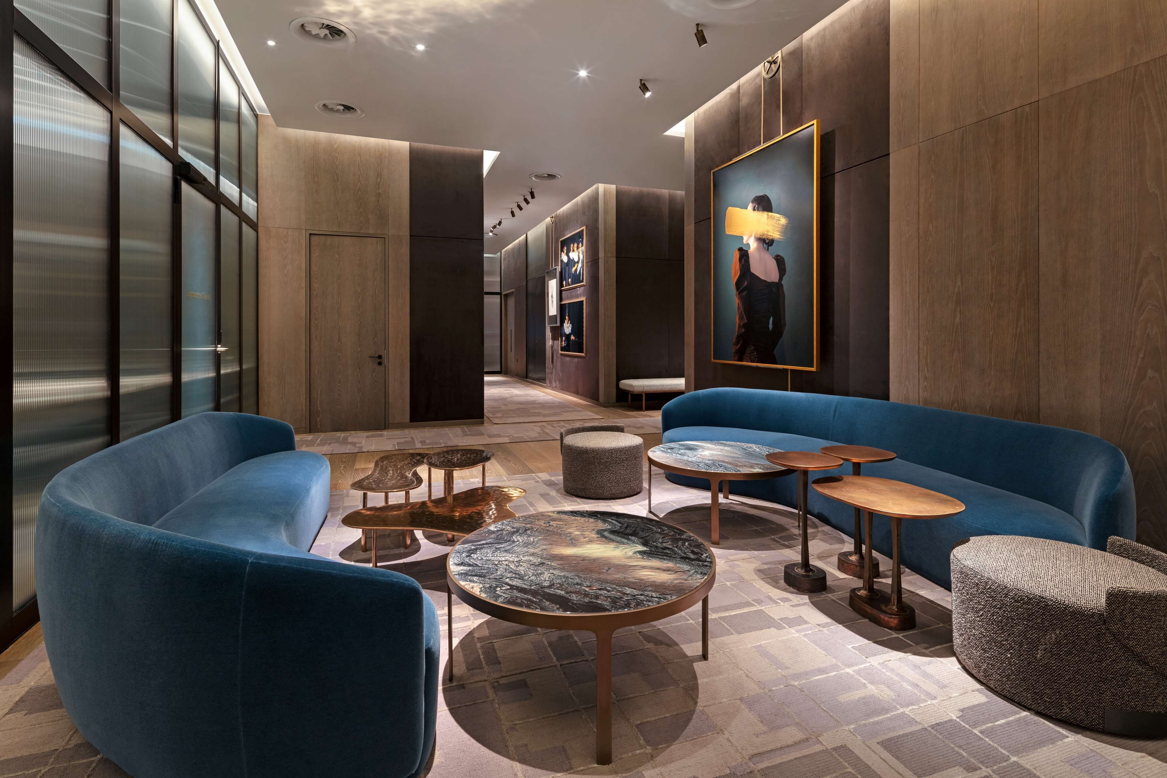 Un hall d’entrée moderne avec des canapés bleus, des tables rondes et une grande œuvre d’art encadrée au mur.