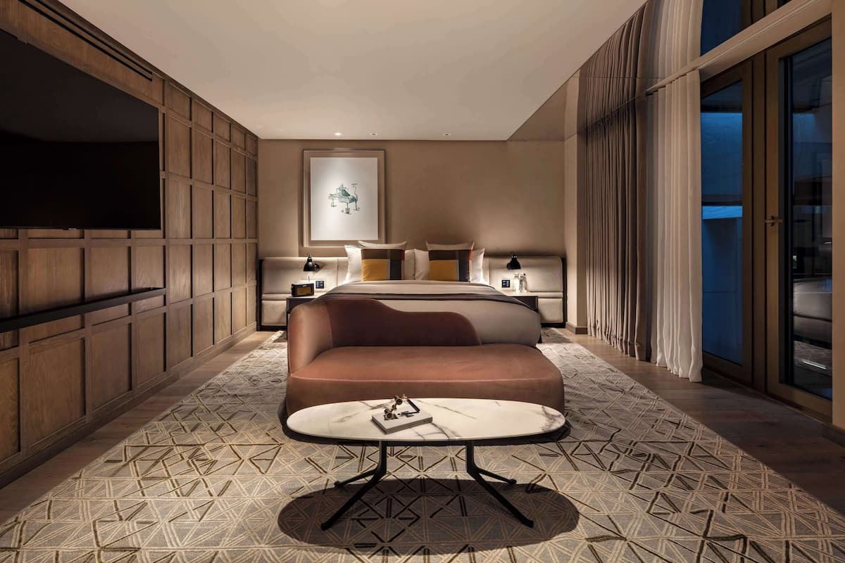 A modern hotel room with a large bed, a sofa, a small table, and a TV.