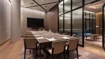 A conference room with a long table, chairs, a flat-screen TV, and a glass partition.