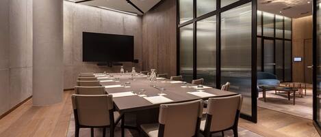 A conference room with a long table, chairs, a flat-screen TV, and a glass partition.
