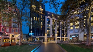 Un edificio moderno con facciata in vetro, un ingresso centrale e una passeggiata circostante.