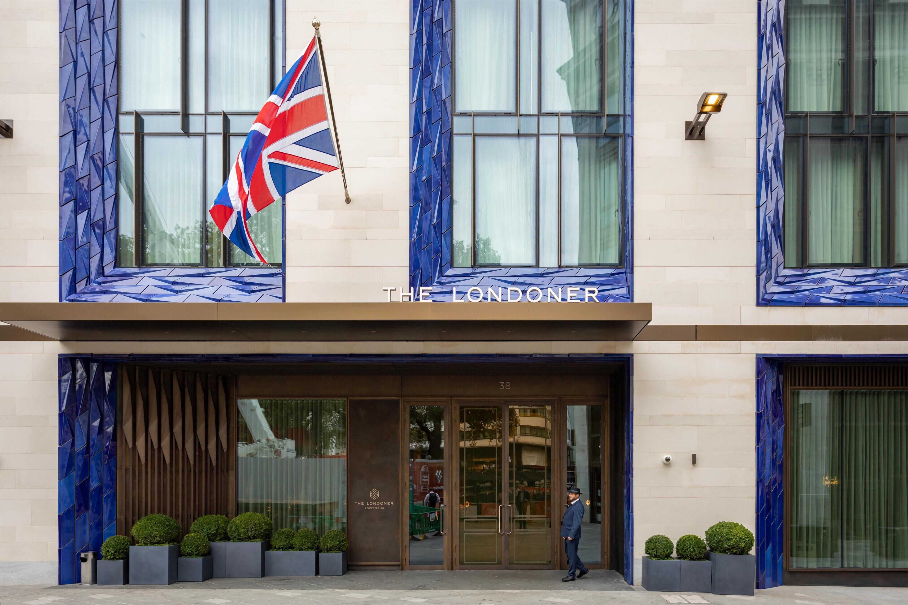 A hotel entrance with a flag, glass doors, and a name sign.