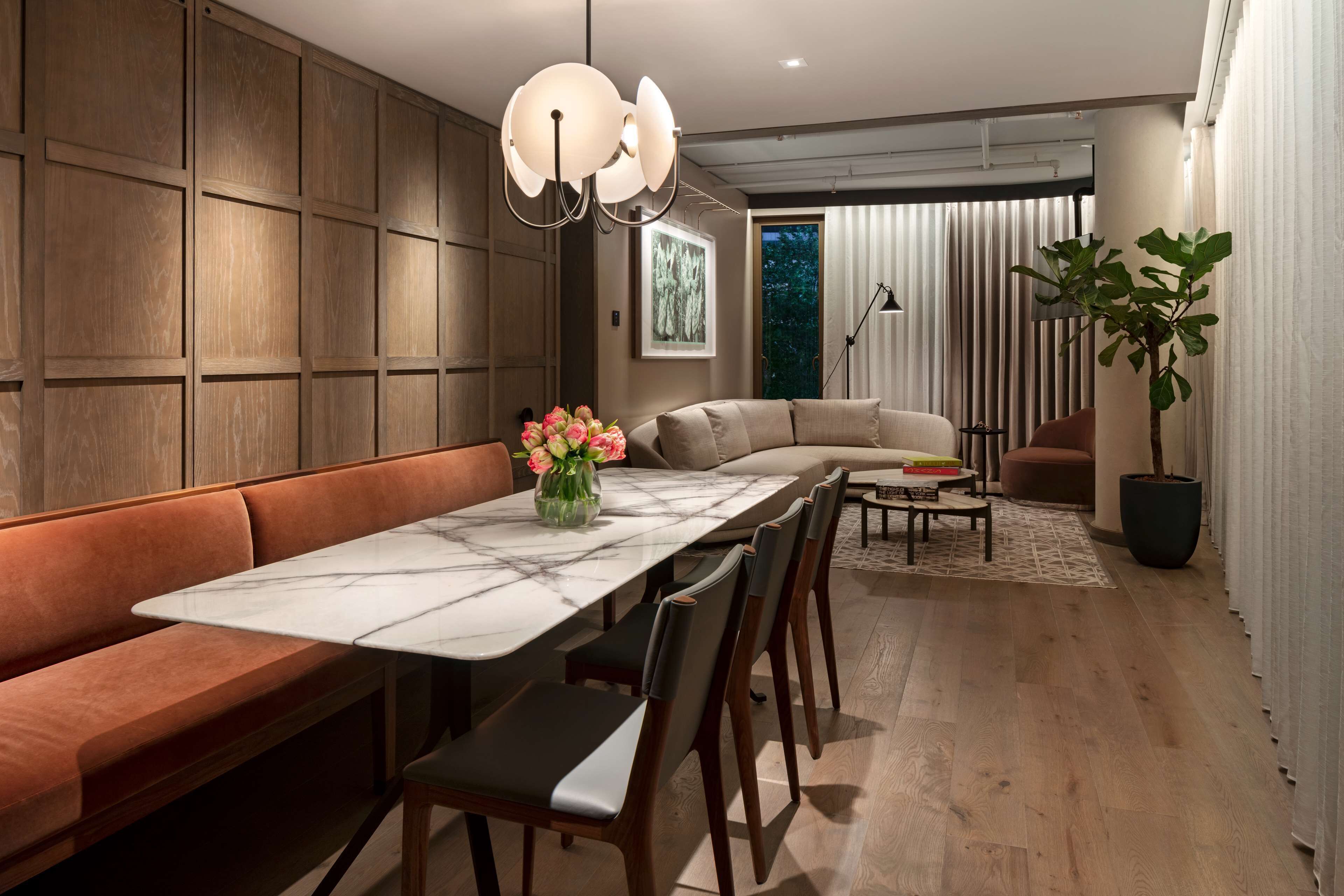 A modern dining area with a marble table, cushioned bench, and wooden paneling.
