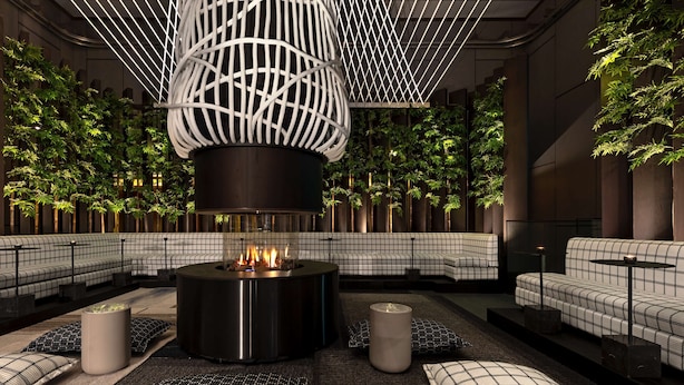 Area lounge moderna con elemento centrale a camino, posti a sedere e verde verticale.