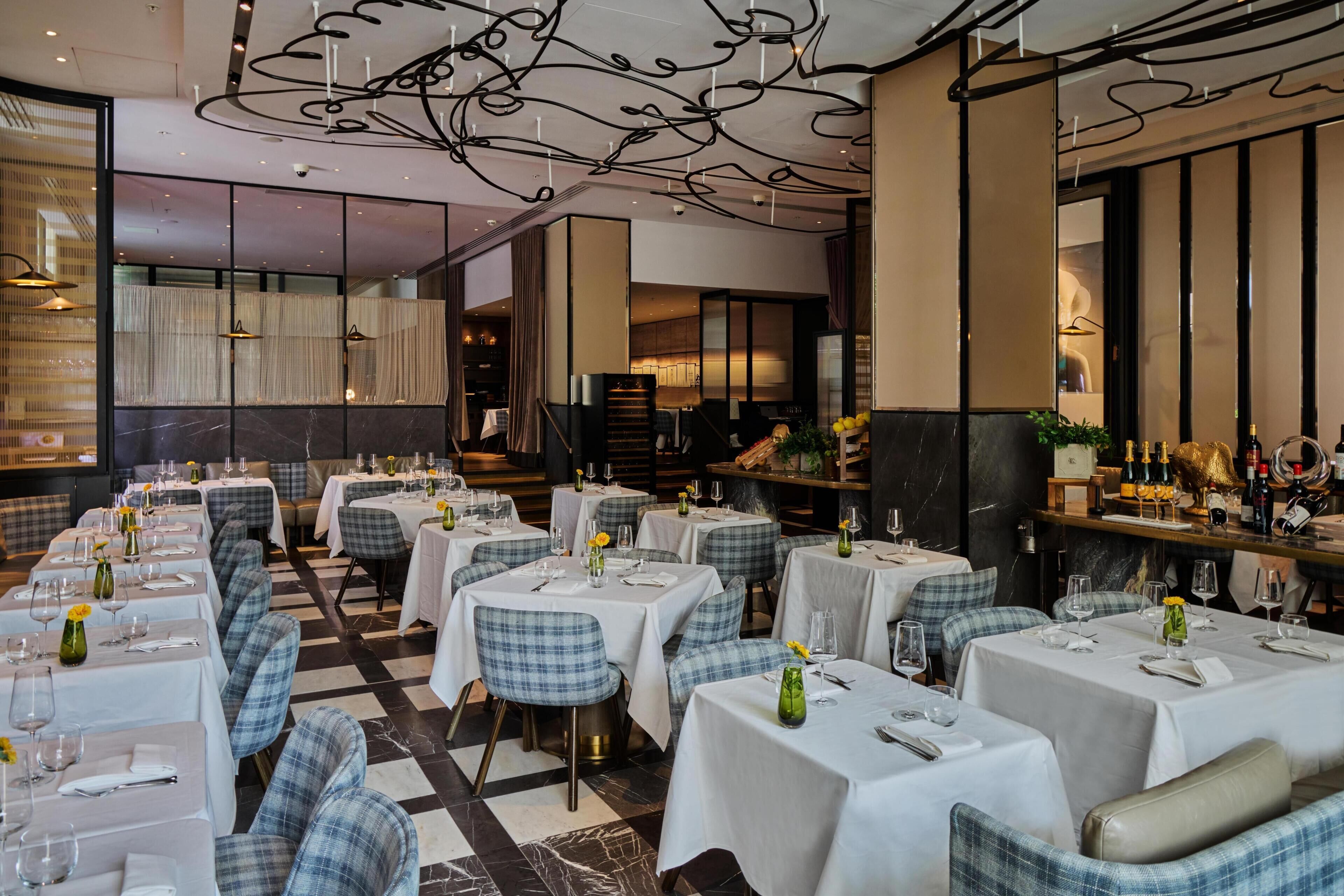 En restaurang med flera bord som är dukade för middag, med ett rutmönstrat golv och en bardisk med flaskor.