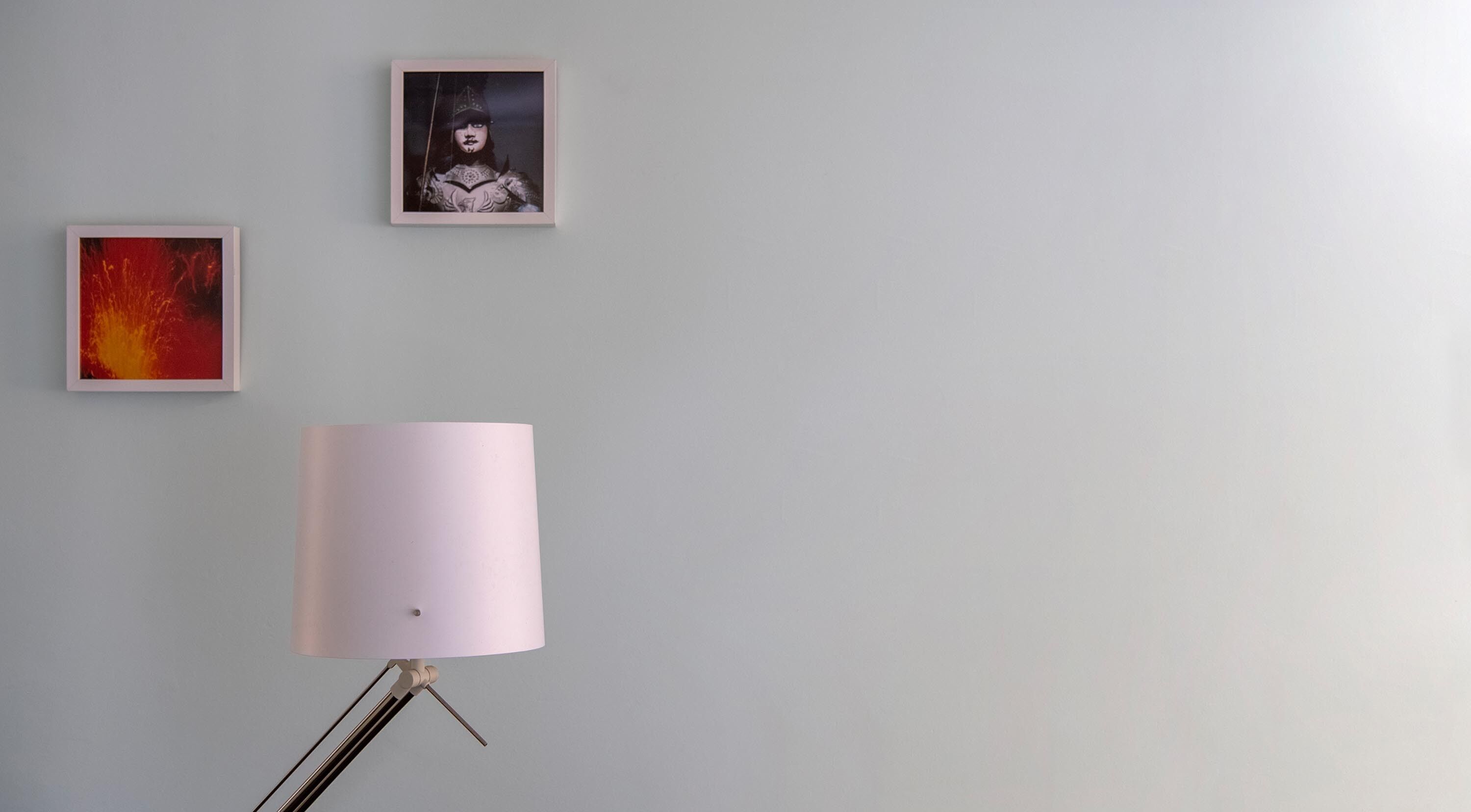 A room with a white floor lamp on a tripod stand, a framed abstract painting on the left, and another framed painting above it.
