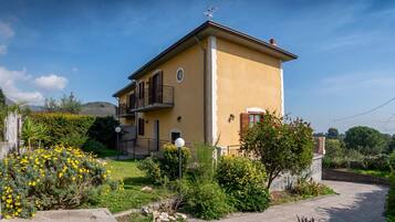 Una casa gialla a due piani con un balcone, immersa nel verde e sotto un cielo sereno.
