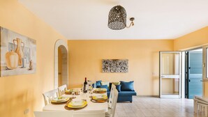 Et spiseområde med et hvidt bord dækket til fire personer, en blå sofa og en moderne lysekrone.
