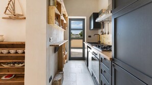 Een smalle keuken met houten planken, een grote koelkast en een uitzicht door de deur.