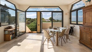 Een moderne eetruimte met een glazen tafel en stoelen, een houten kast en uitzicht op de omgeving.