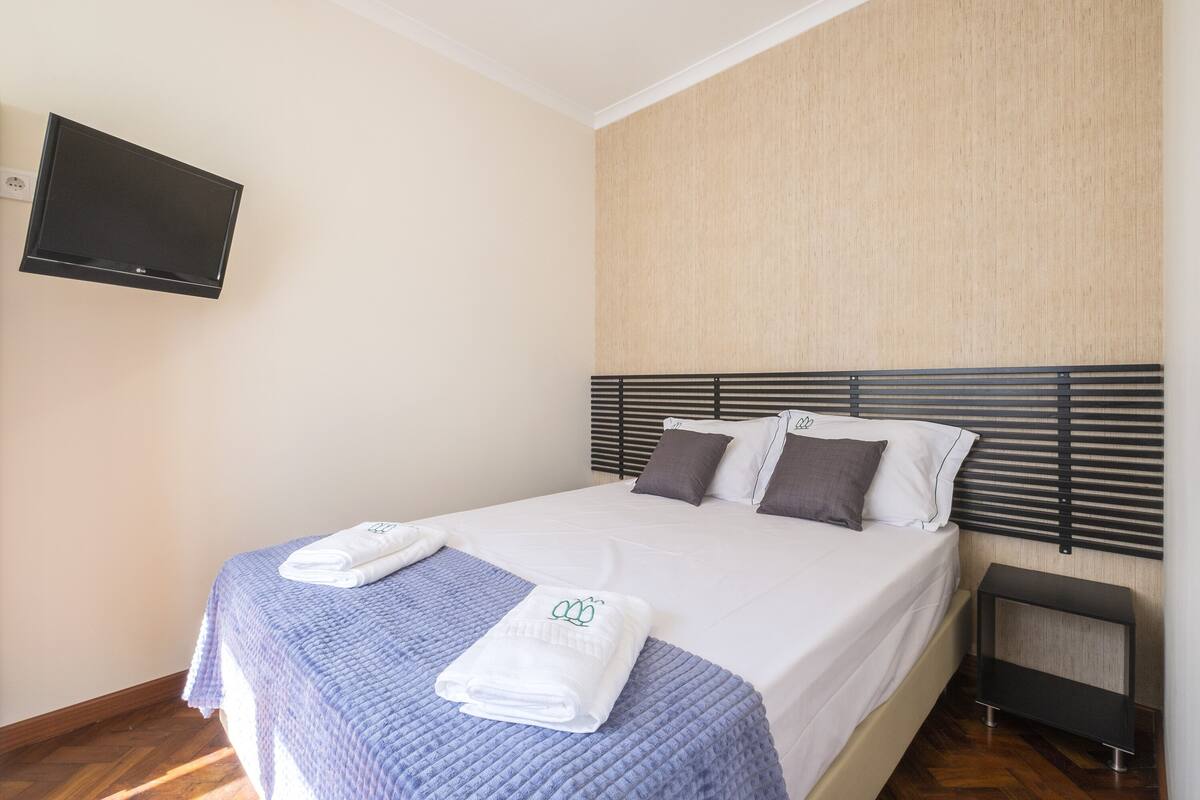 A neatly made bed with a blue blanket, white pillows, and a folded towel on the bed.
