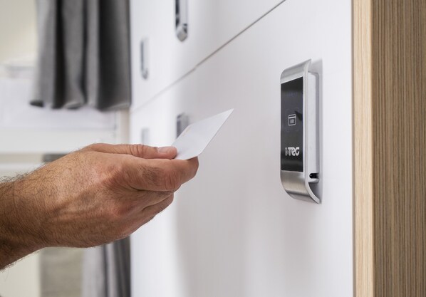 Une main insère une clé dans un lecteur de carte à puce moderne, en métal, situé sur une porte.