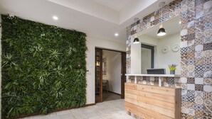 A bathroom with a green vertical garden wall, a wooden vanity with a mirror, and patterned tiles on the walls. - Passal Hostel (Ponta Delgada)