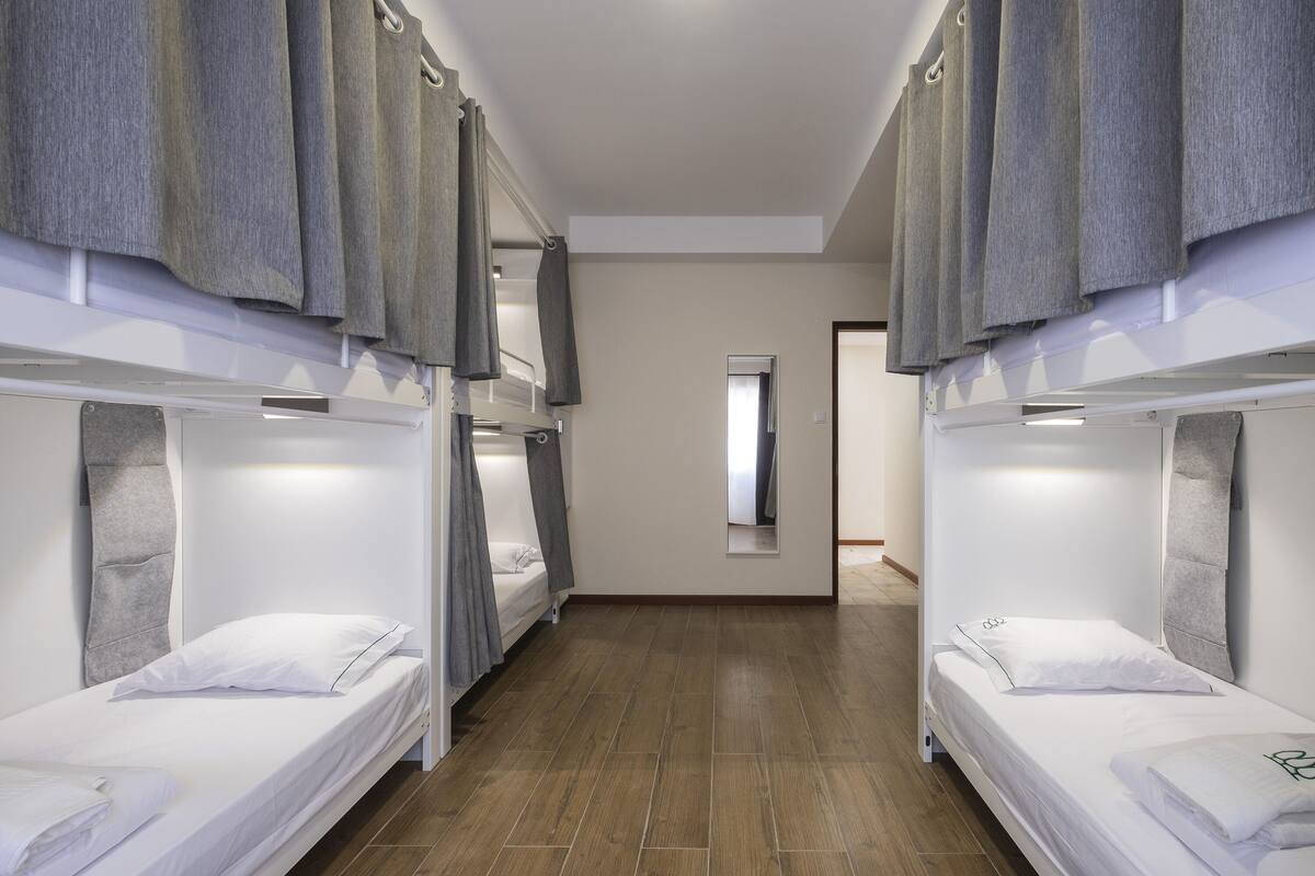 A hotel room with bunk beds, a small window, and a wooden floor.