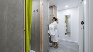 A person in a white robe standing in a hallway with a mirror, wooden beams, and a green curtain. - Passal Hostel (Ponta Delgada)