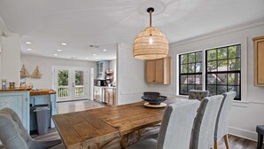 A spacious dining area with a wooden table, grey upholstered chairs, and a woven pendant light.