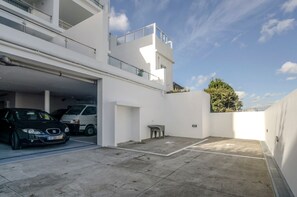 A modern building with a garage parking area, a small outdoor seating area, and a tree in the background.