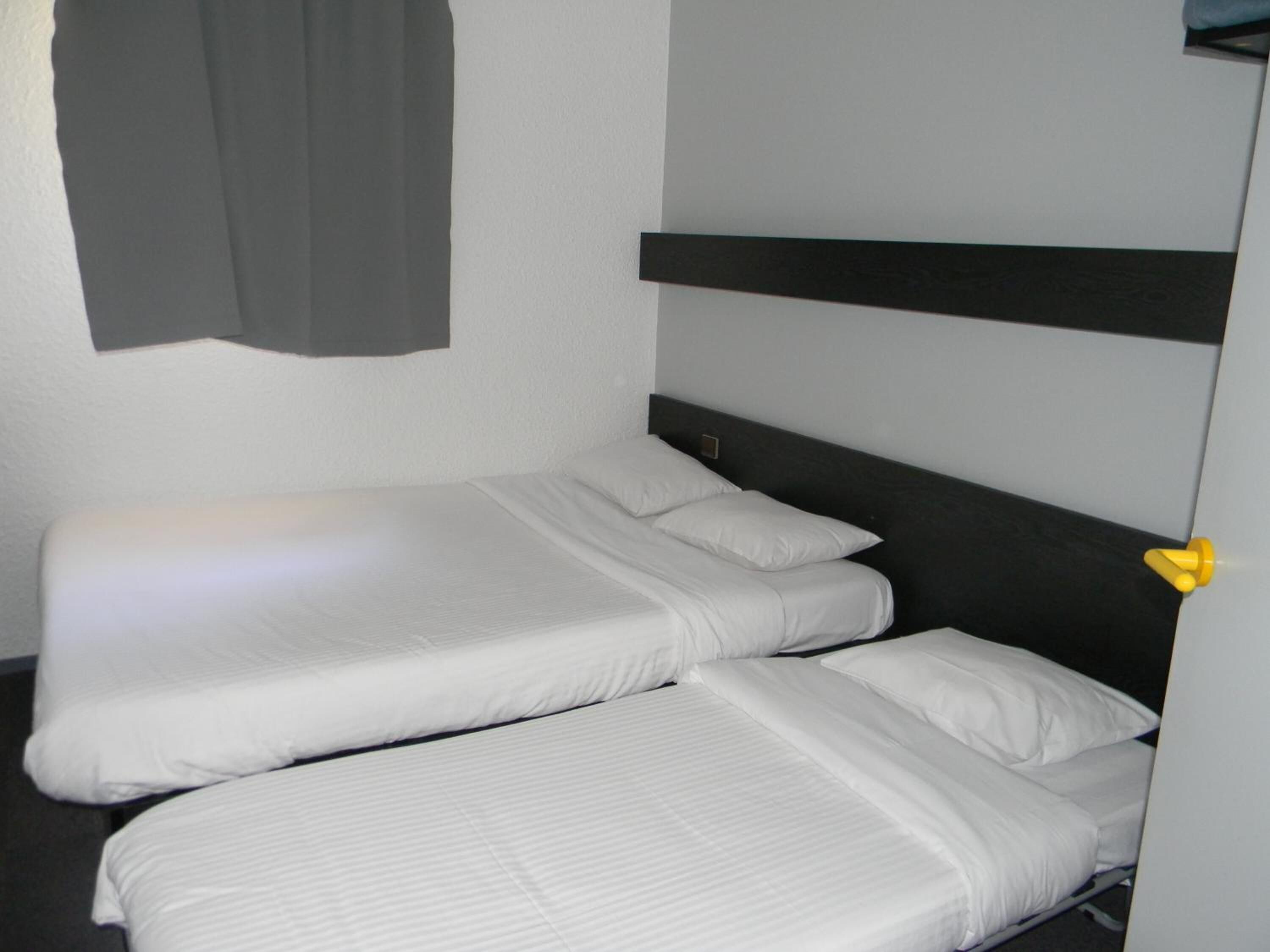 A single bed with white bedding in a room with a dark headboard and a gray curtain.