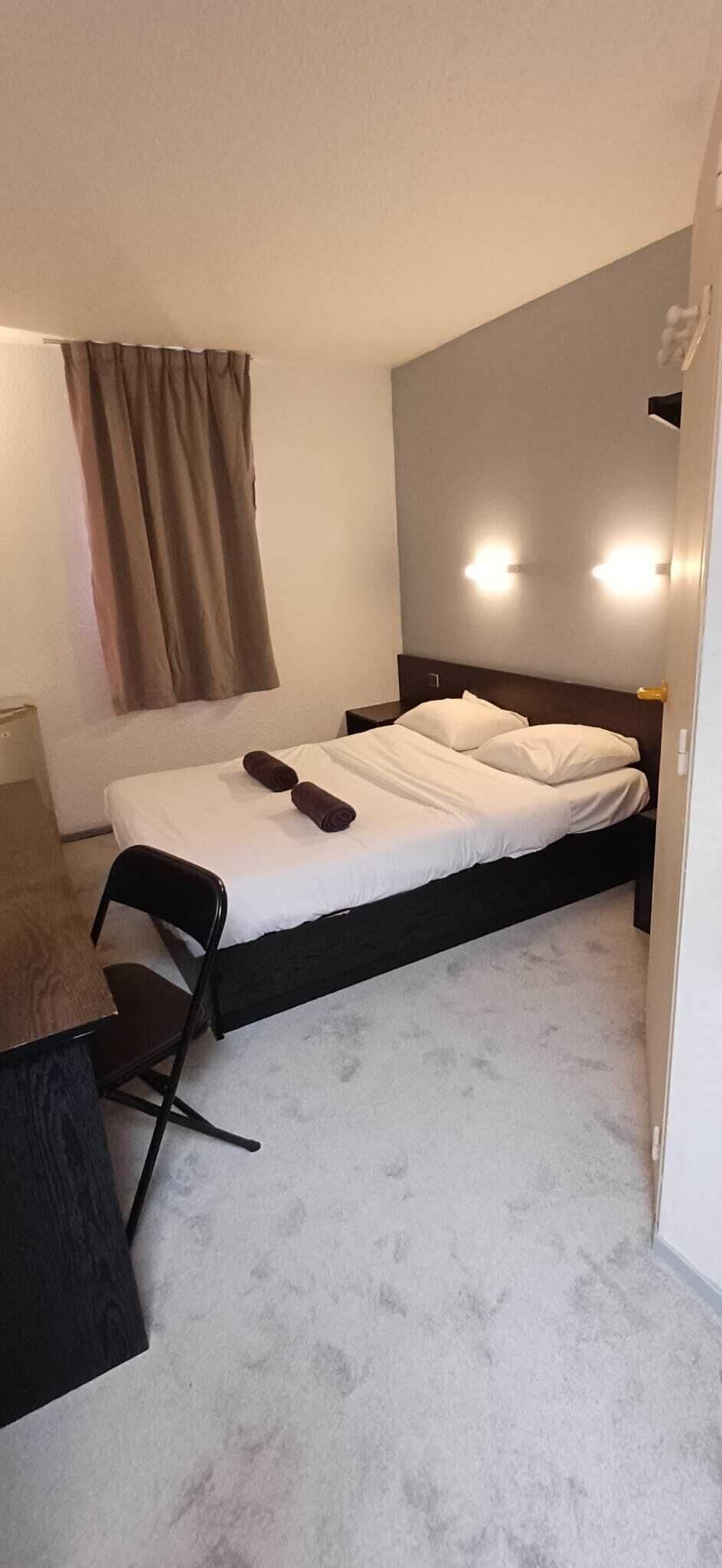 Un letto singolo con testiera in legno, una scrivania con una sedia e una finestra con tende.