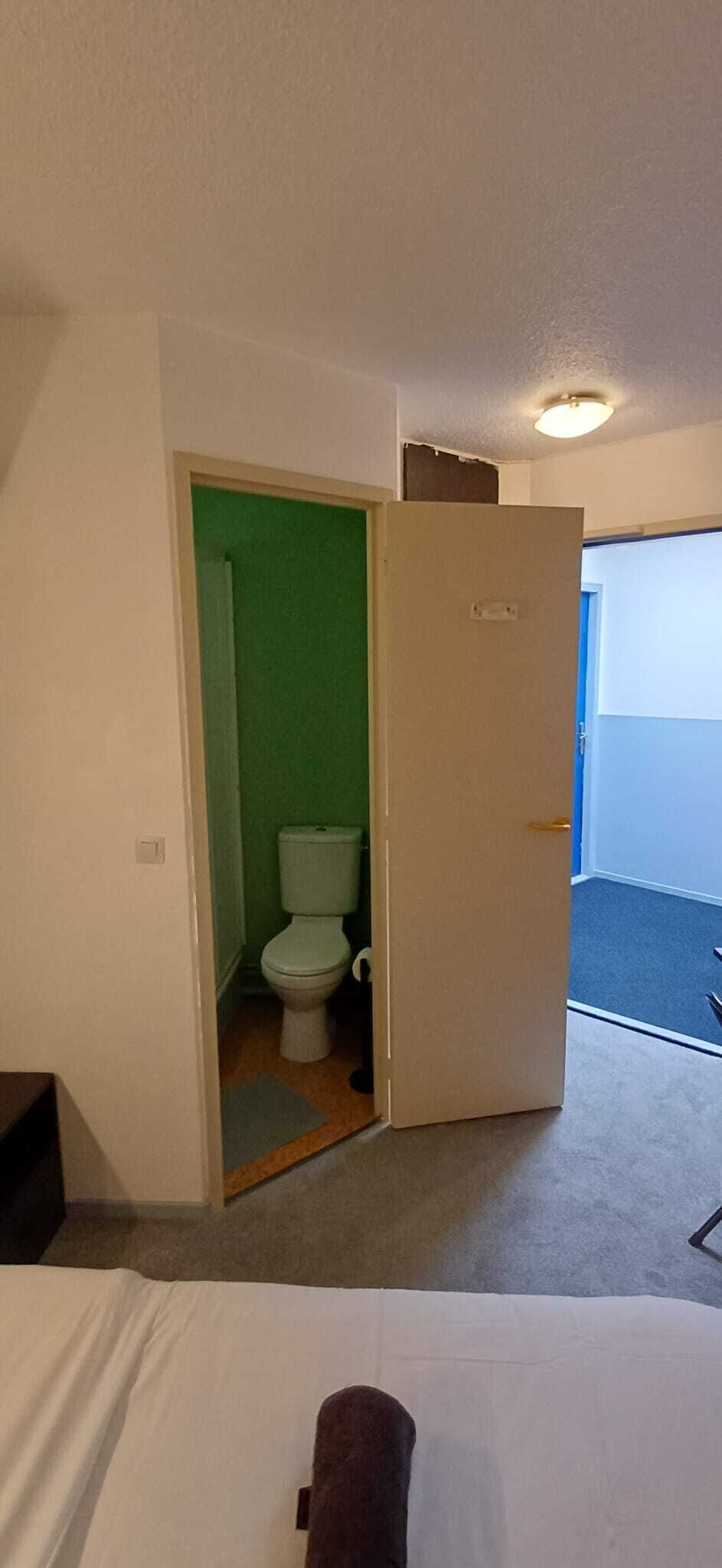 A hotel room with a bed, a door leading to a bathroom, and a view of the outside.