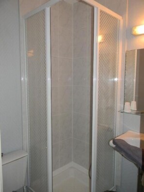 A corner shower with a glass door, a white sink, and a mirror above the sink.