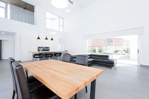 Een ruime, moderne keuken met een houten eettafel en stoelen, een zwarte leren bank en hanglampen.