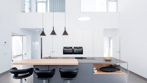 Et moderne køkken med en central ø, barstole, hængende lamper og integrerede hårde hvidevarer.