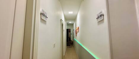 A narrow hallway with white walls, a green LED strip lighting, and a patterned rug at the end.