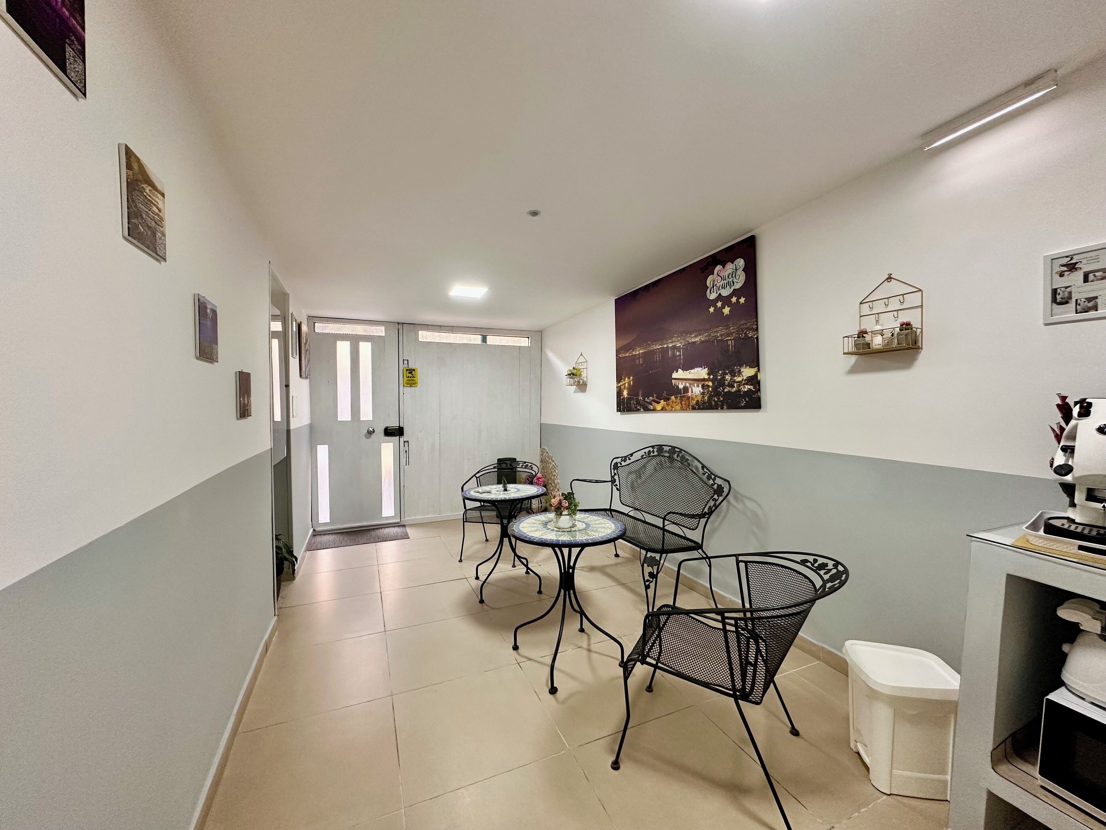 A hallway with a door leading to a room, a small table with chairs, a trash bin, and a wall-mounted shelf with hooks.